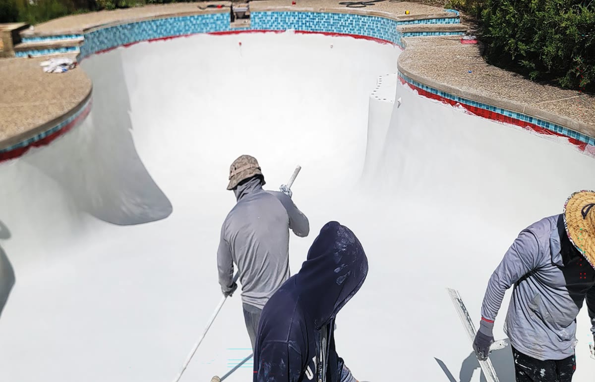 Crew applying polymer concrete plaster to swimming pool interior